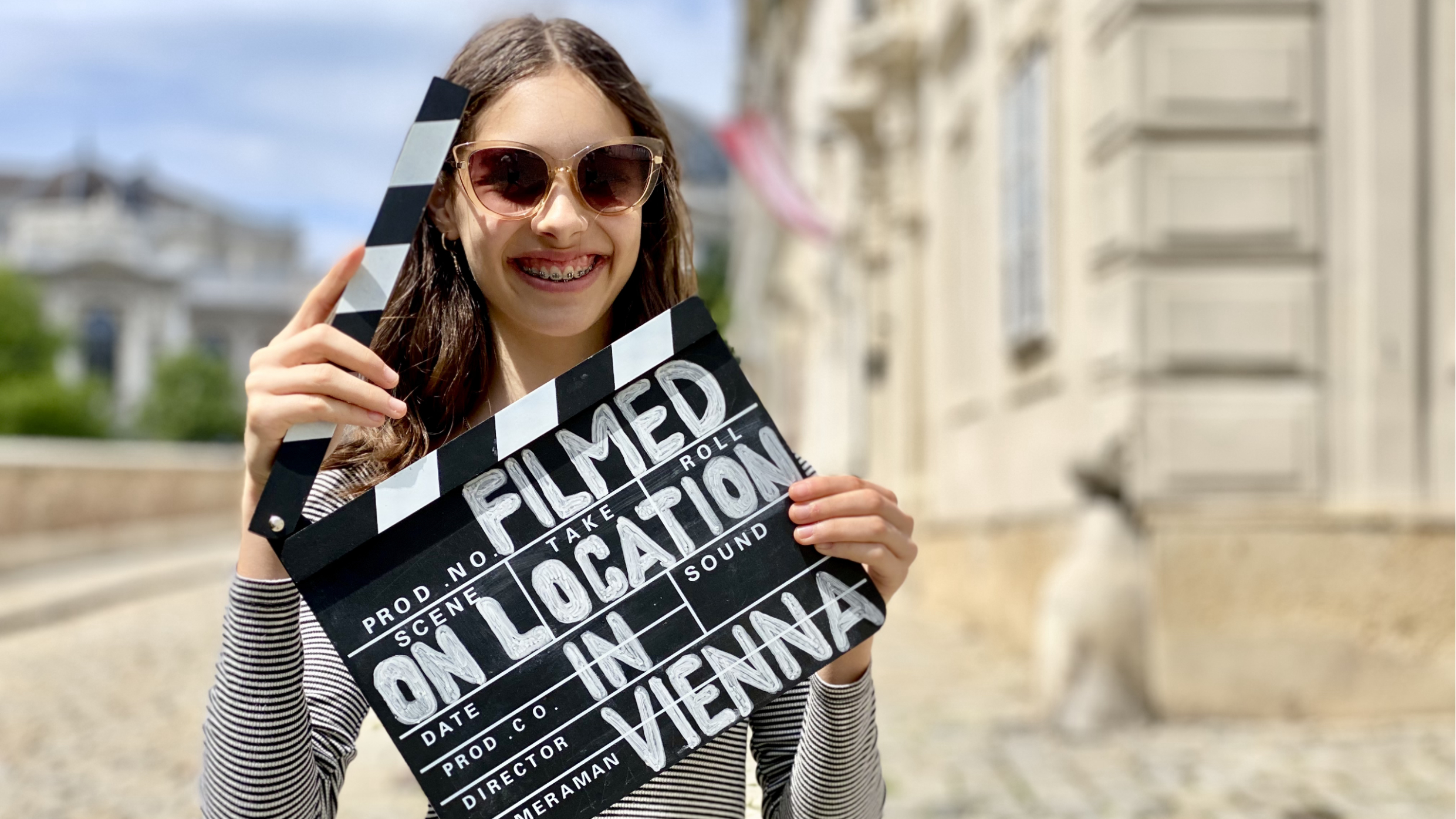 Lächelndes Mädchen mit einer Filmklappe in der Hand auf der Mölker Bastei. Auf der Klappe steht: Filmed on Location in Vienna