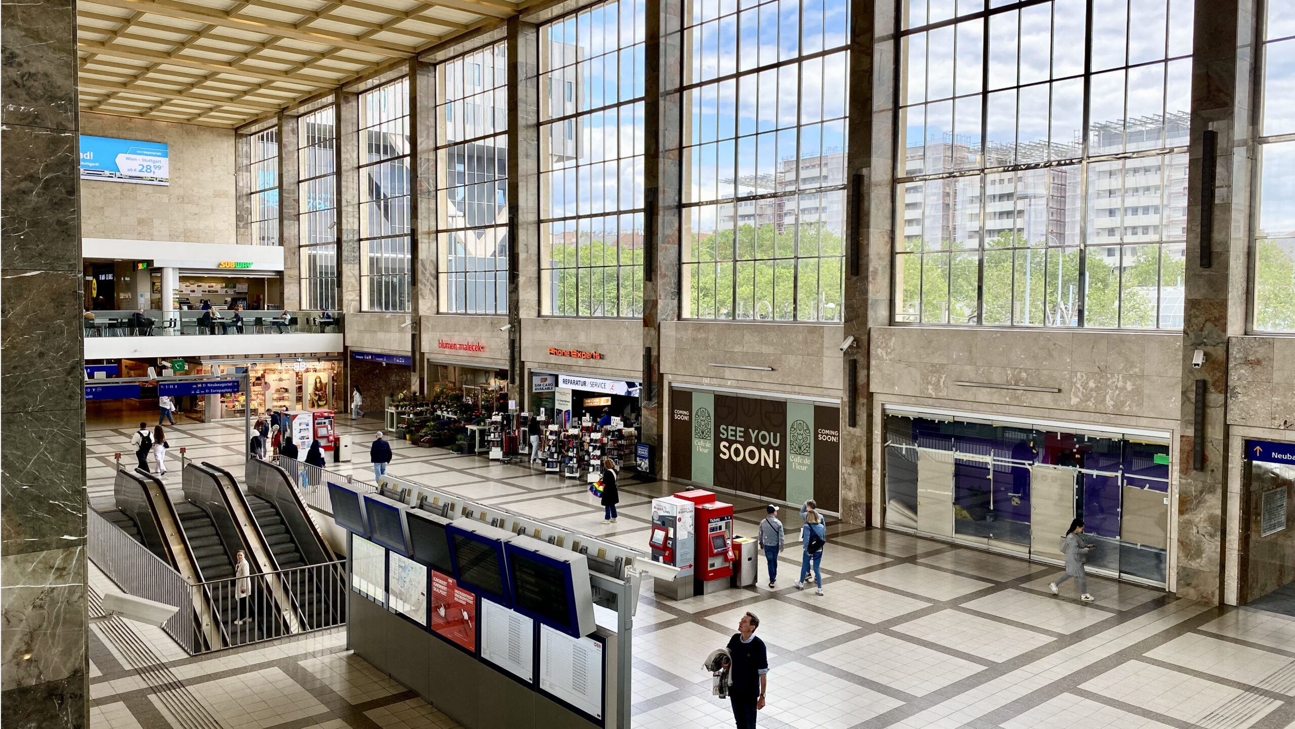 Die Eingangshalle des Wiener Westbahnhofs ist geprägt von einer großen Glasfassade. Einige Geschäfte. Mid-century Design.